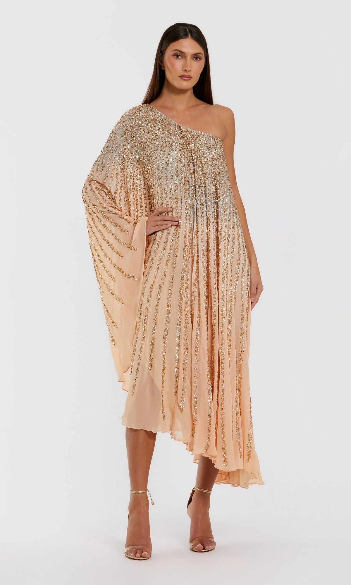 A woman wearing the Tea-Length Party Dress: Mac Duggal 6204 in champagne gold, featuring a one-shoulder neckline, knee-length hem, elegant gold sequin embellishments, and a draped sleeve stands against a white background—an exquisite look that showcases signature Mac Duggal elegance.